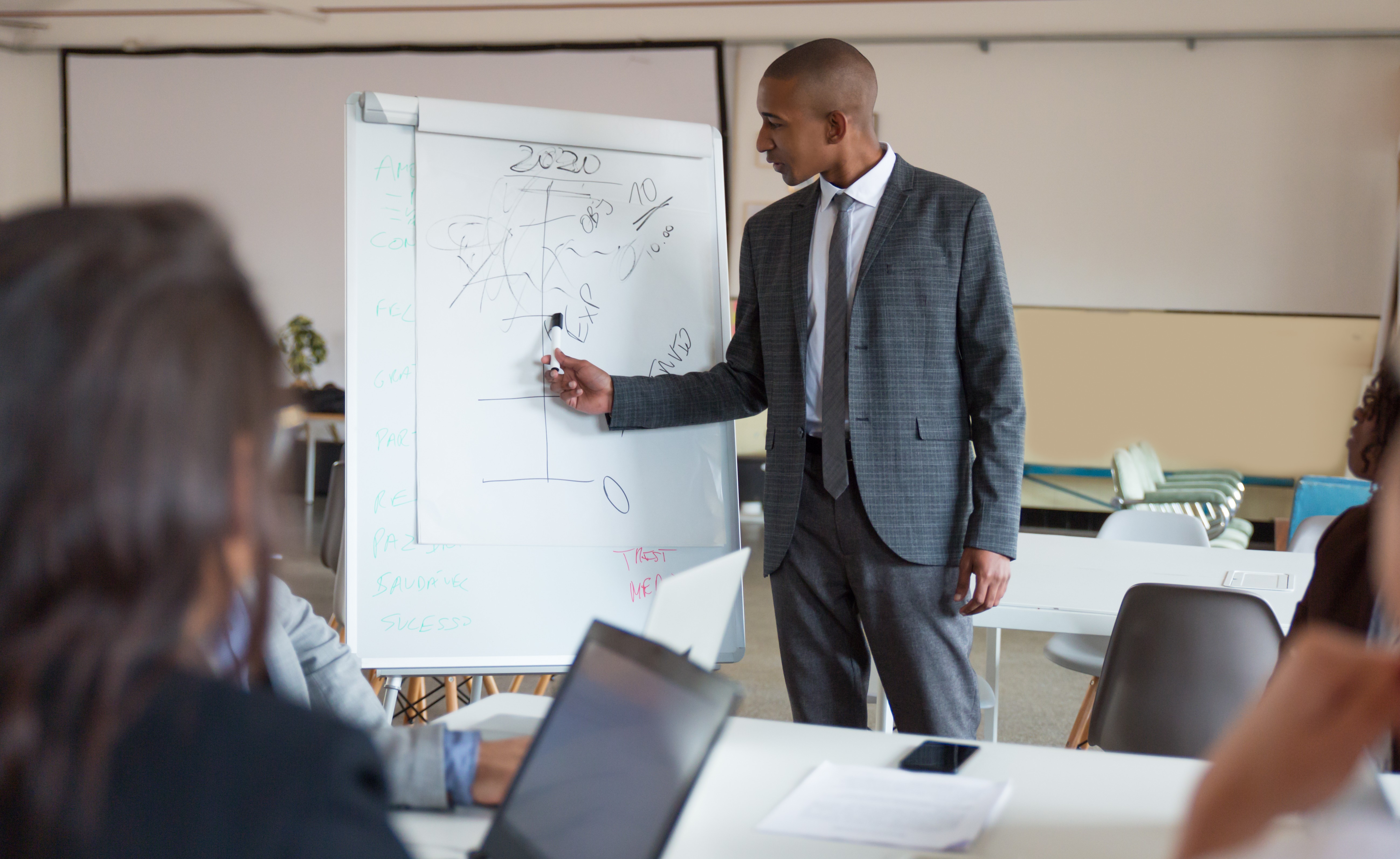 Confident speaker talking and pointing at whiteboard. Group of employees discussing ideas during presentation of new project at briefing. Business meeting concept
